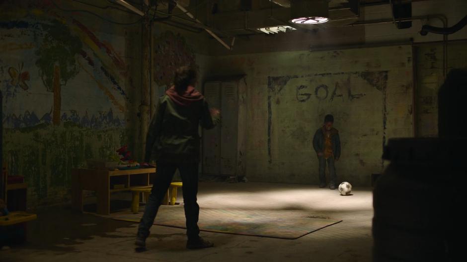 Ellie and Sam play soccer agains a goal painted on the wall.