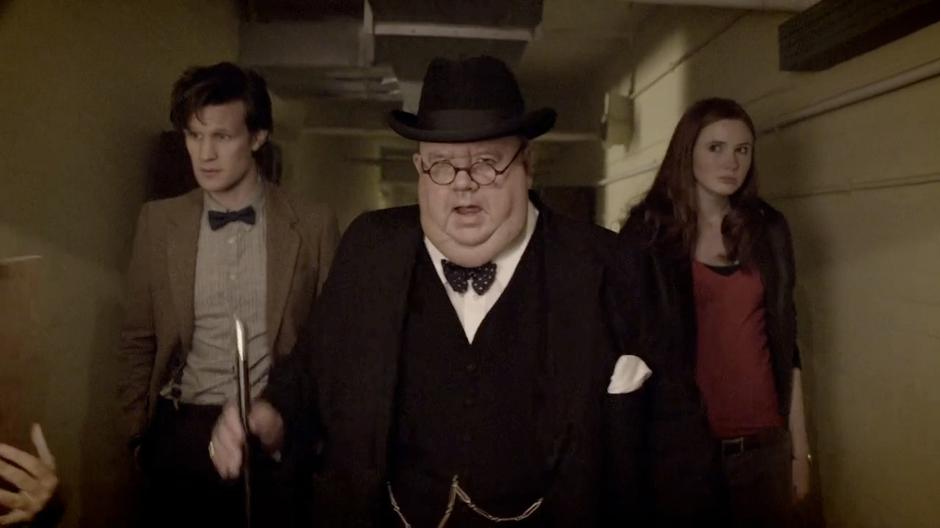 Churchill, Amy, and the Doctor walk through the bunker hallway.