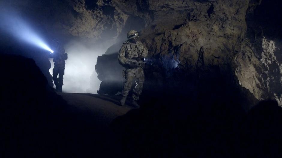 Two soldiers search through a side cavern.