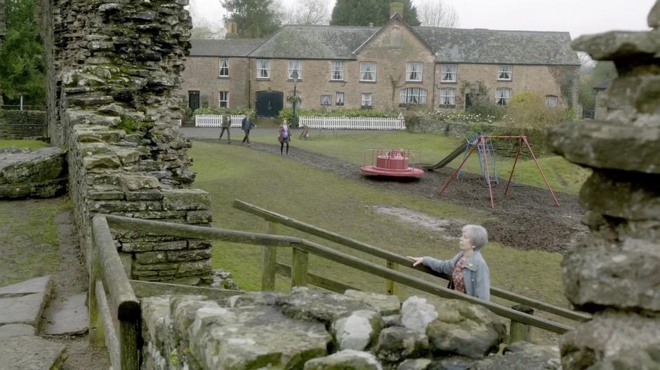 An old lady walks into the castle ruins while the group goes to the playground.