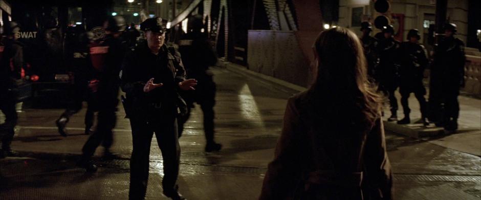 A police officer tries to stop Rachel Dawes from crossing the bridge.