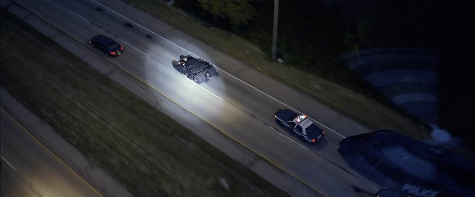 A police helicopter spotlights the Batmobile.
