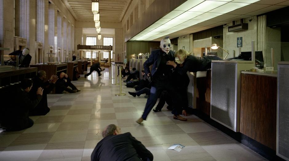 A masked man pulls a bank teller over the counter.