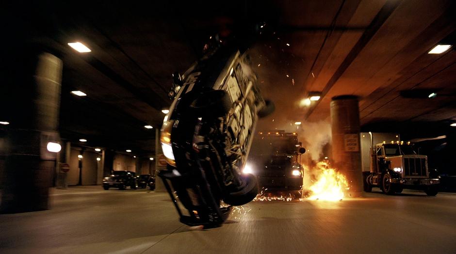 A police car flips over after being shot with a rocket by the Joker.