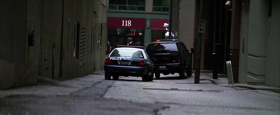 The police vehicle carrying Reese drives out of the alley.