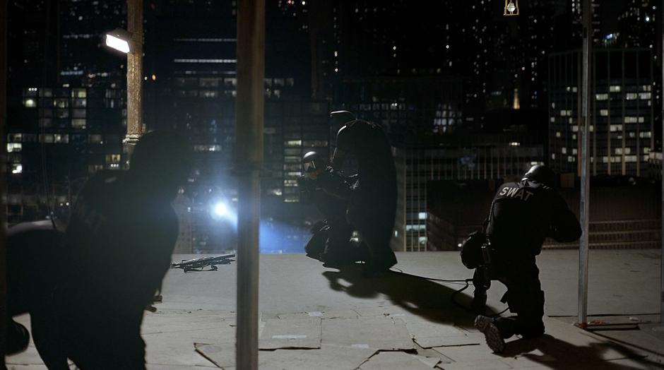 Batman ties up a SWAT team member and prepares to knock several of them from the building.