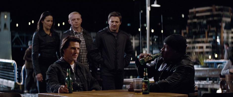 Ethan Hunt and Luther Stickell are talking at a table and are approached by the rest of the team.