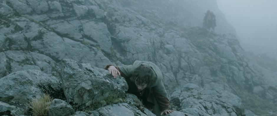 Frodo and Sam climb over rocks while lost in the fog.