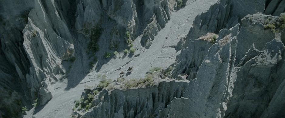 Aragorn, Legolas, and Gimli ride through the rocks of the Dimholt Road.