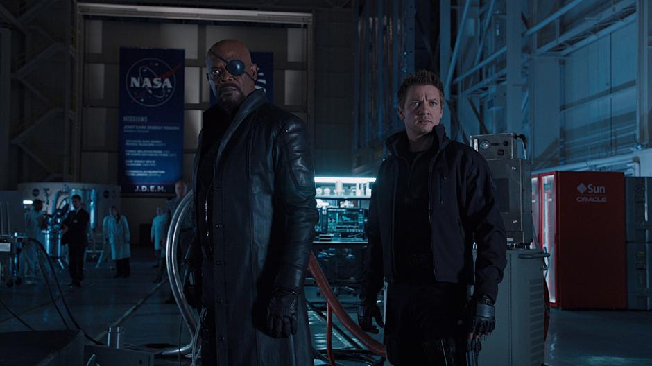 Nick Fury and Hawkeye look at the pedestal where Loki is appearing.