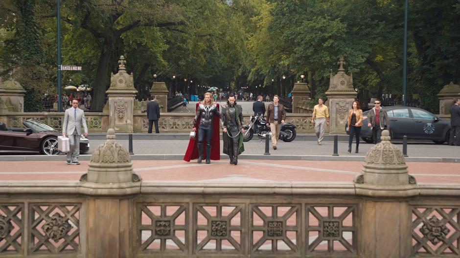 Thor walks Loki to the teleport point while the rest of the Avengers approach from across the street.