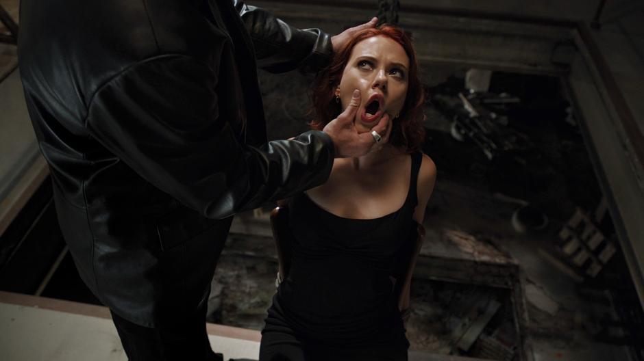 One of the thugs holds Black Widow's mouth open while leaning her back over a several floor drop.