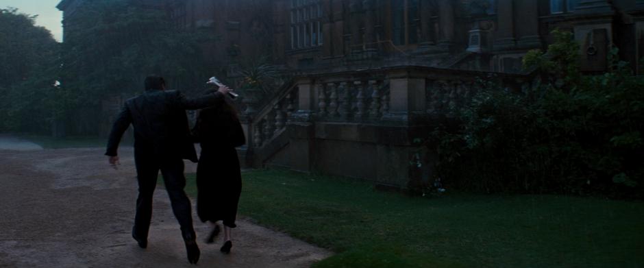 Bruce and Miranda run to the side door of the manor in the rain.