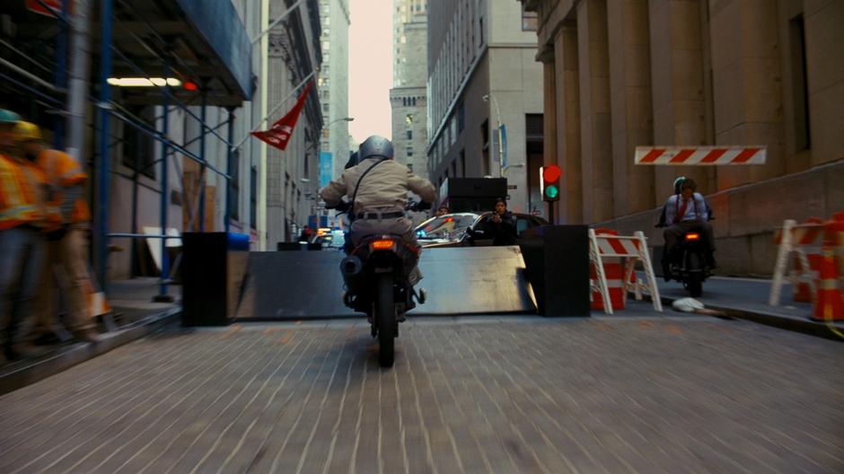 One of Bane's men drives his motorcycle past the police cordon.