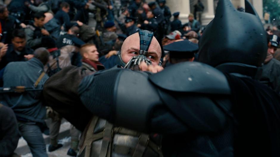 Bane stops one of Batman's punches inside the melee on the steps of the building.