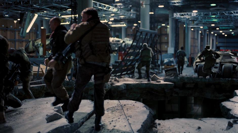 Bane's thugs storm up into the storage warehouse through the hole blasted in the floor.