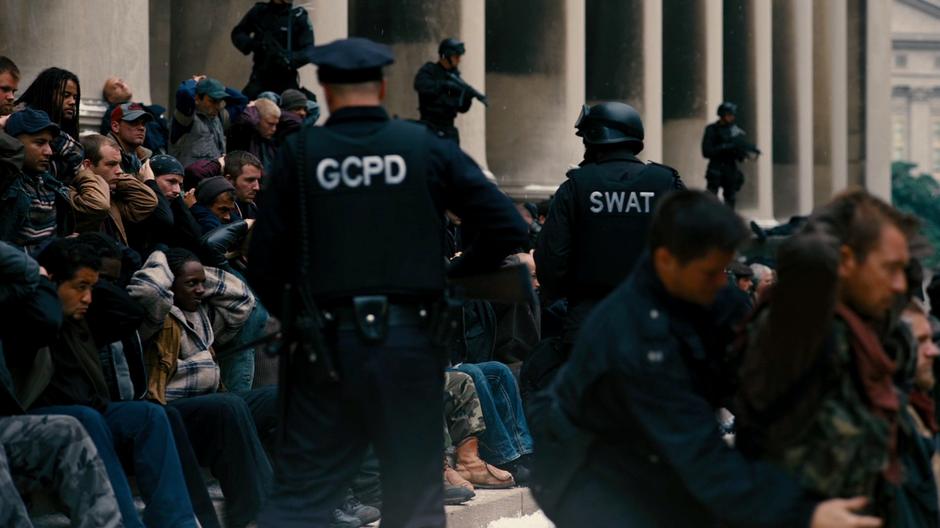 Police officers watch over the captured members of Bane's army on the steps of the building.