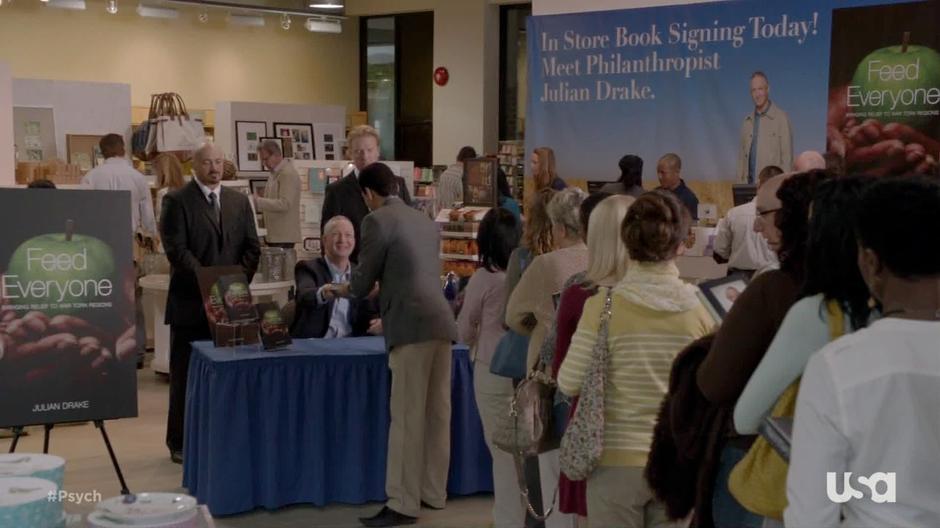 Julian Drake signs books while his bodyguards stand behind.