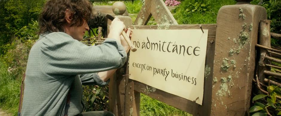 Frodo puts up the party sign on the gate to Bag End.