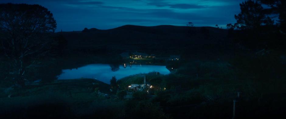 Nighttime establishing shot of Hobbiton looking across the pond towards the Green Dragon.