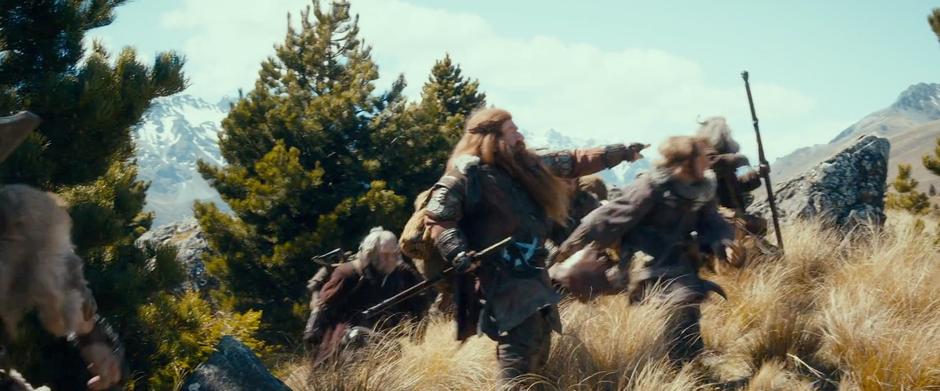 Gloin points ahead while the dwarves run through the tall grass while being chased by the wargs.