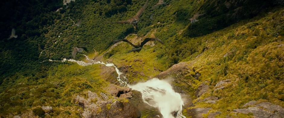 The eagles fly over a waterfall and down into a valley.