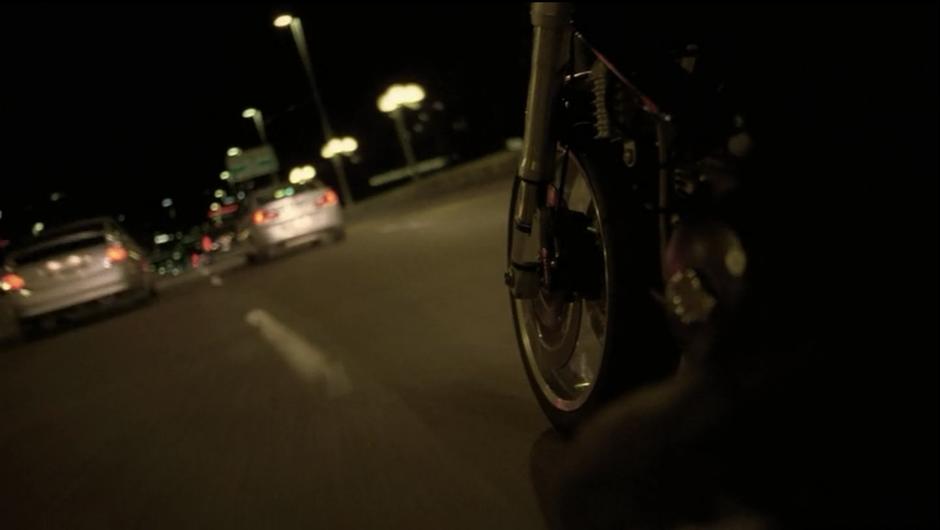 Sam races his motorcycle through traffic over a bridge.