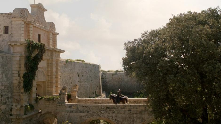 Catelyn and Ser Rodrik ride across the bridge to the gate.