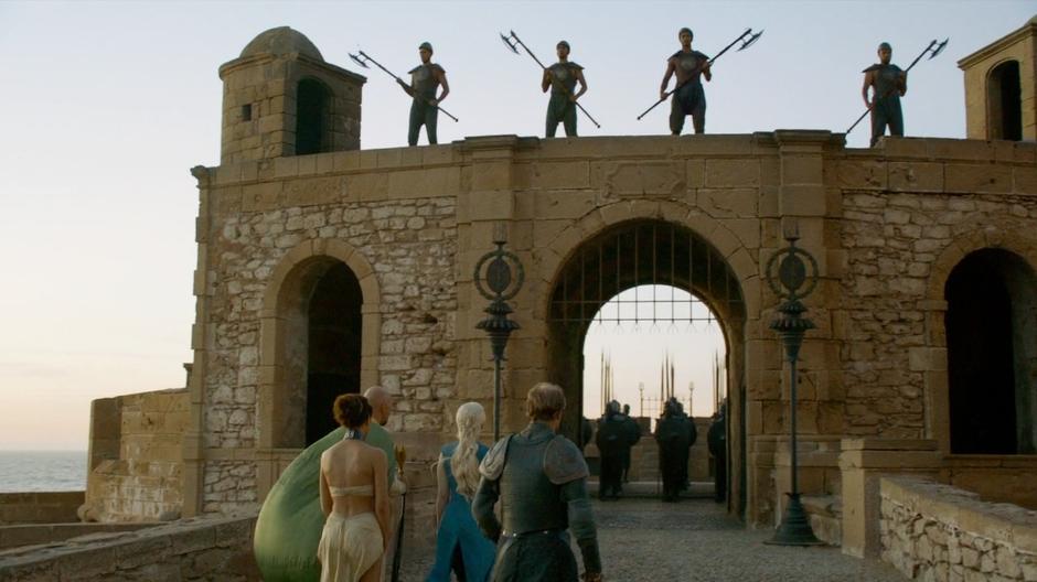 Daenerys and her group walk into the market underneath some Unsullied guards.