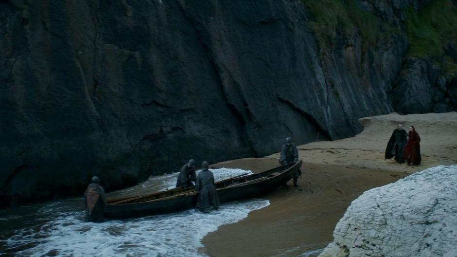 Stannis and Melisandre walk down to the shore while her boat is put into the water.