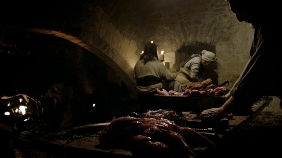 A cook cuts up meet for the banquet in the Winterfell kitchen.