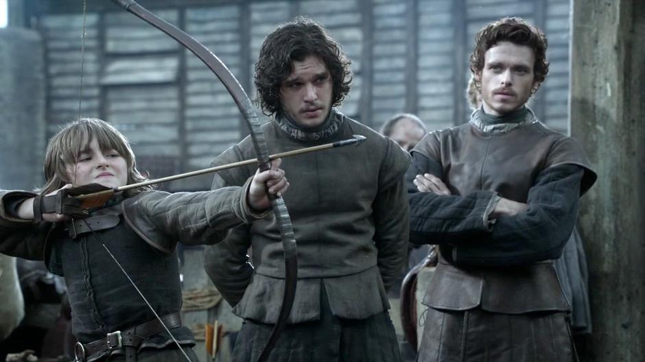 Bran gets ready to shoot an arrow white Jon Snow and Robb look on.