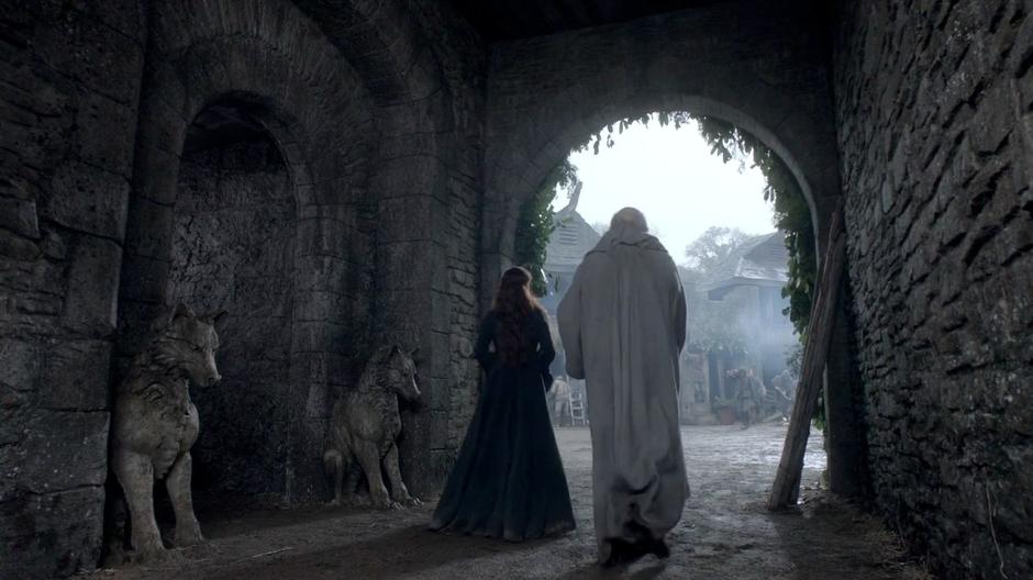 Catelyn and Maester Luwin walk out from under the arch into the courtyard.