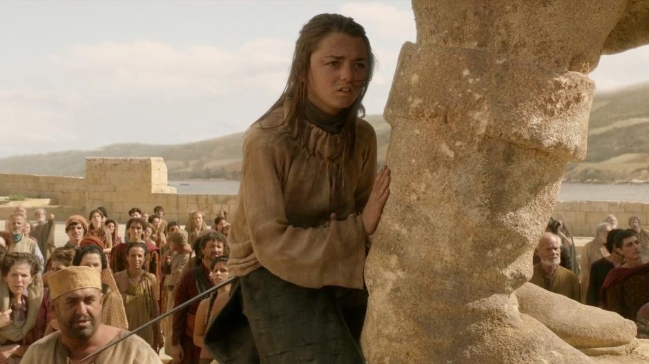 Arya watches her father's confession from atop a statue in the square.