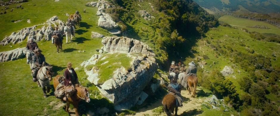 The company rides down a small path into a valley outside of the Shire.