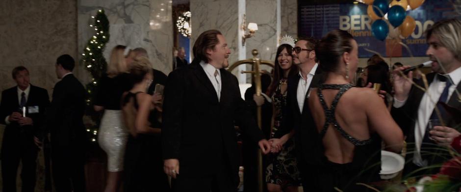 Happy looks back at Tony while escorting him and Maya through the lobby.