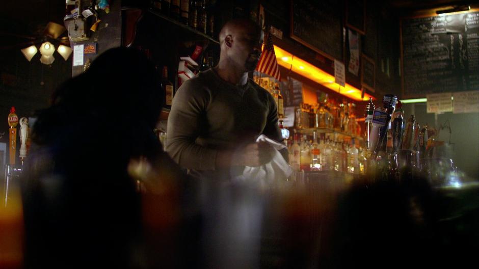 Luke polishes a glass behind the bar as Jessica sits at a stool.