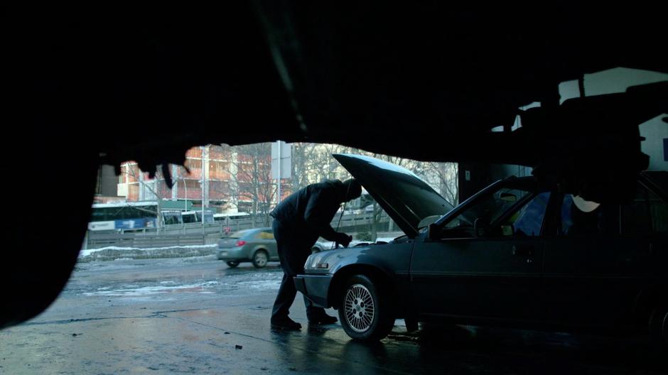 A worker leans over the open hood of a car.
