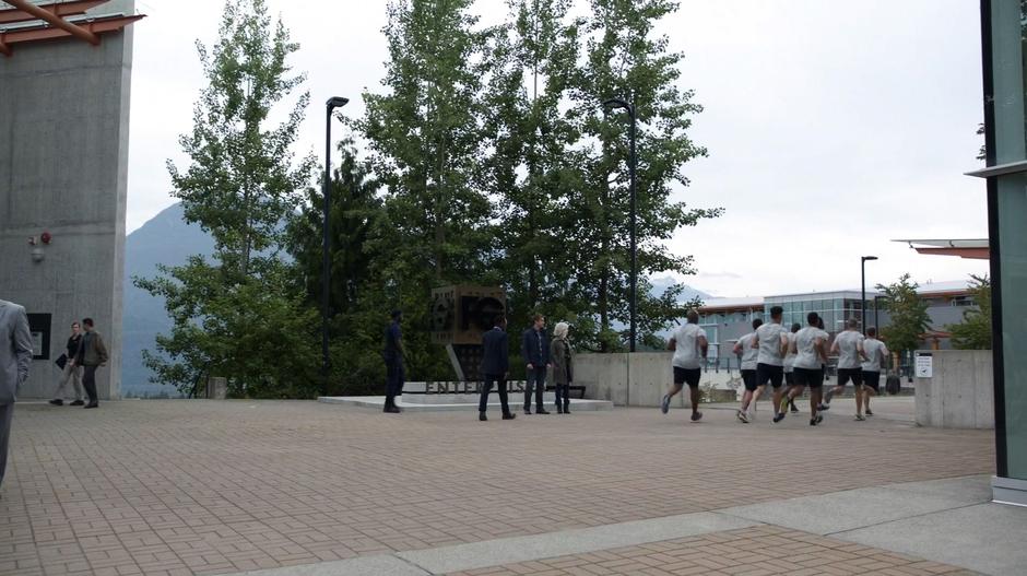 Clive approaches Liv and Major while a group of the paramilitary employees jogs off around the corner.