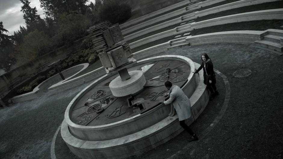 Penny drags one of the pieces of the shield off the Poison Room's fountain while Sylvia stands by.