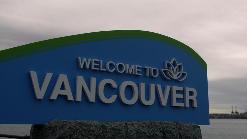 A Welcome to Vancouver sign sits in front of the water.
