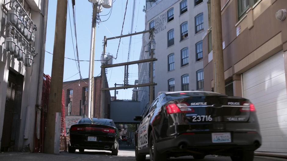 A squad car pulls up next to the car where Liv and Clive are staked out in the alley.