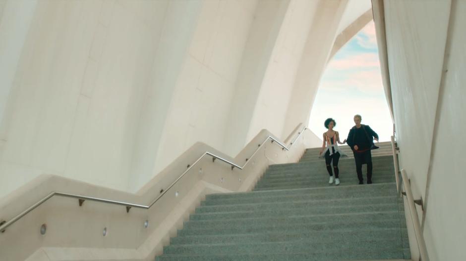 Bill and the Doctor rush down some stairs while Bill wonders why the robots aren't following very quickly.