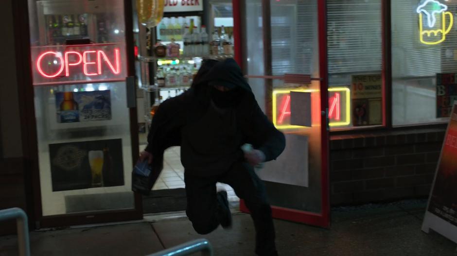 A robber runs out of the door of the liquor store.