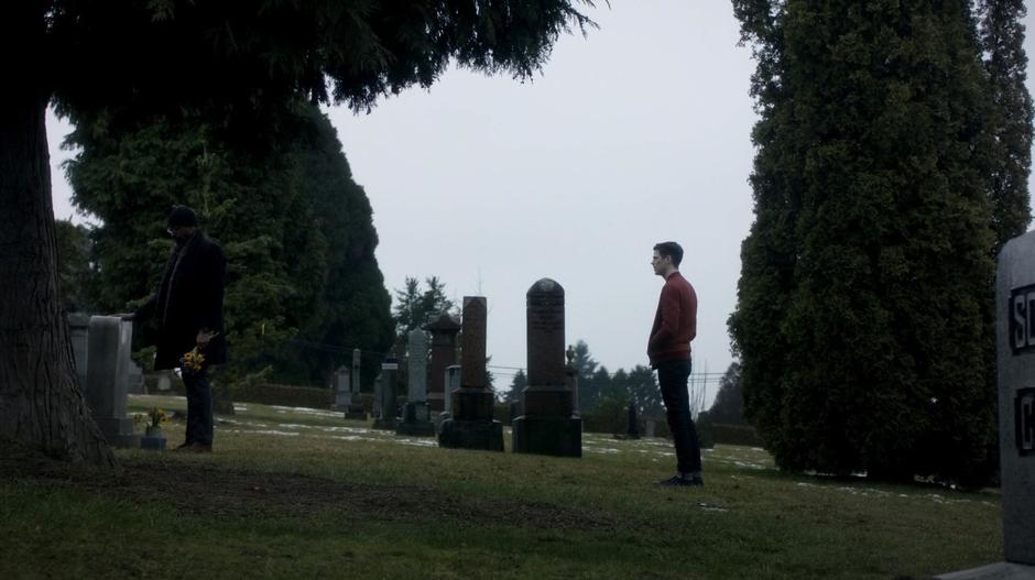 Joe stands in front of Iris's grave with a handful of flowers as Barry approaches him from behind to talk.
