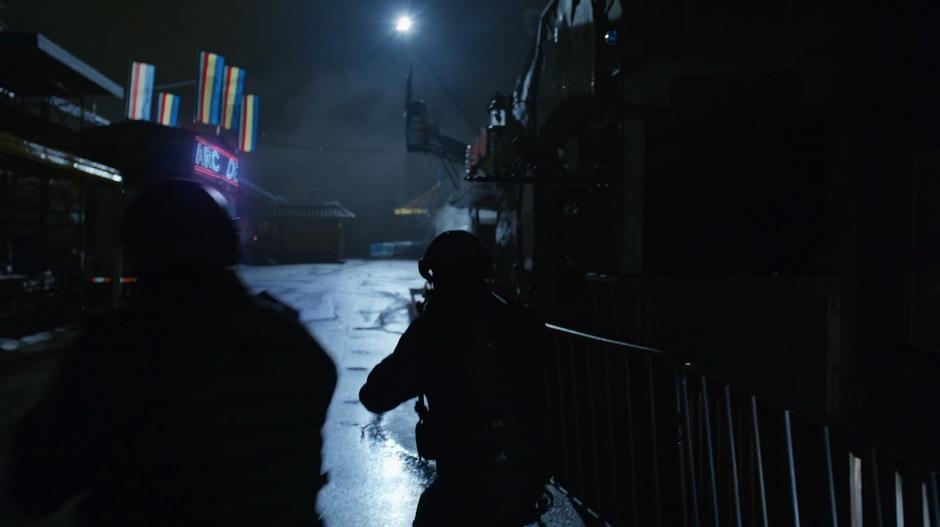 A pair of A.R.G.U.S. agents walk through the carnival towards the arcade.
