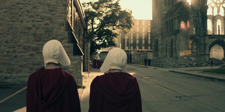 Ofglen and Offred walk down the street towards the shell of a church.