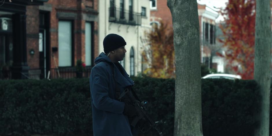 A guard stands on the street with a large gun while looking across the street.