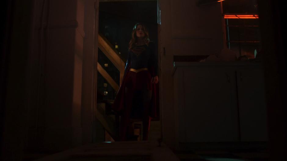 Kara kicks down the door to the house and looks inside.