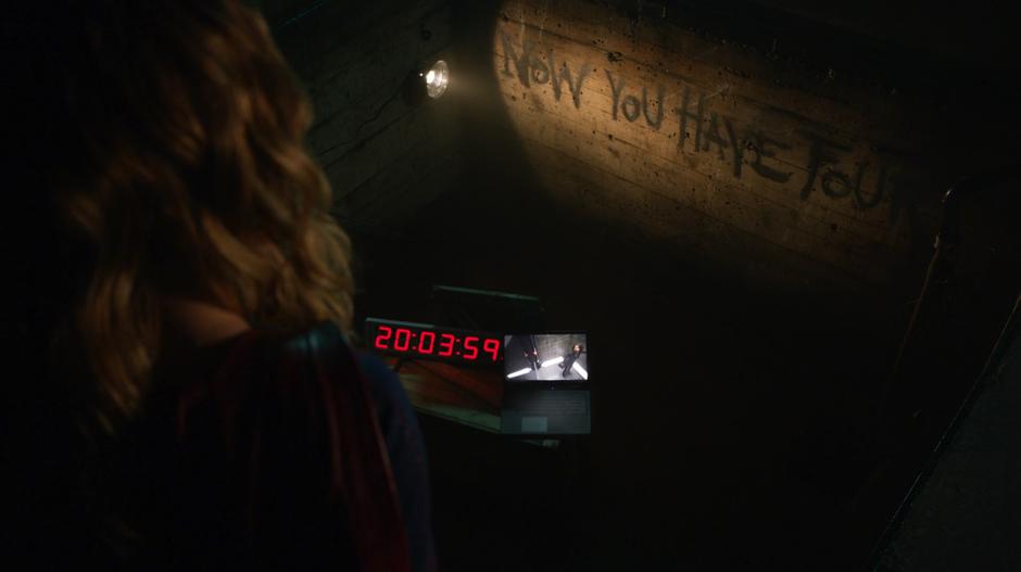 At the bottom of the pit Kara sees a message from Rick Malverne scrawled on the wall, a countdown timer, and a laptop showing video of Alex in the cell.